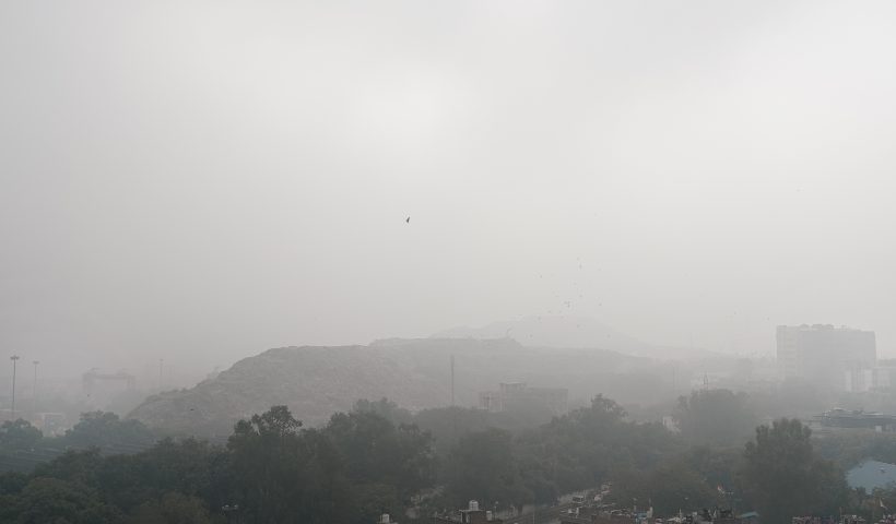 A view of the Okhla landfill covered in thick fog, highlighting pollution and low visibility in the area.